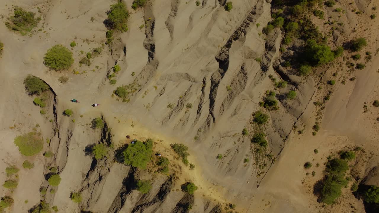 Secuencia de seguimiento aéreo cenital con drones que capta la precisión de una ruta en el norte de España, donde el movimiento geométrico de los ciclistas contrasta con las texturas caóticas y erosionadas del terreno árido