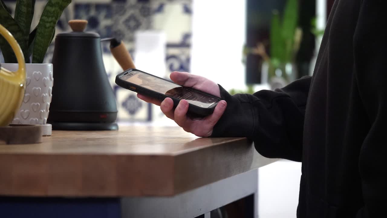 hombre se desplaza a través de las redes sociales en el teléfono inteligente en la cocina y luego se arroja a un lado en cámara lenta