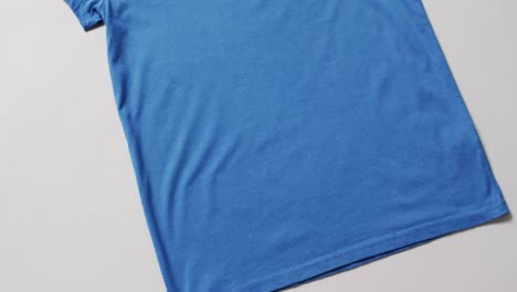 video of flat lay of blue t shirt with copy space on white background