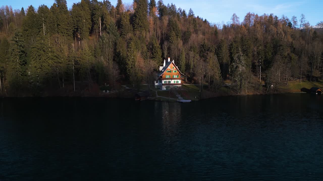 Avvicinamento aereo a una casa sul lago con un riflesso scintillante nell'acqua blu scuro.