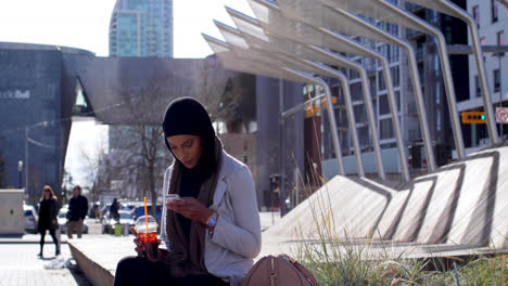 Vista-Lateral-De-Una-Joven-Asiática-Con-Hijab-Usando-Un-Teléfono-Móvil-En-La-Ciudad-4k