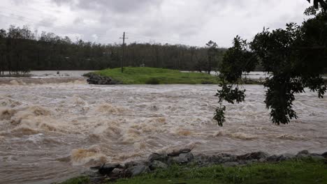 Coomera,-Gold-Coast,-2-De-Enero-De-2024:-Toma-Amplia-De-Agua-Turbulenta-A-Través-De-La-Calzada-Del-Río-Coomera-Bajo-Las-Aguas-De-Las-Inundaciones-De-Las-Tormentas-De-2024-En-Enero