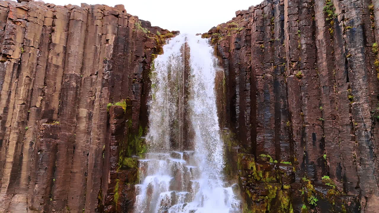 Waterfall in the basaltic cliff. Beautiful rock with the column structure in Iceland. Drone footage.