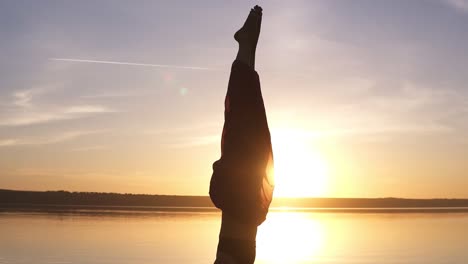 close up footage of a beautiful girl standing stood on her head in yoga asana. sun shines and water on the background