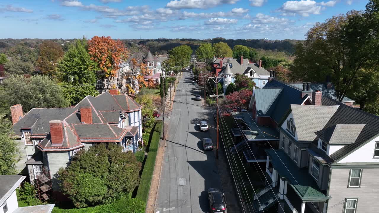 Aerial tracking shot of red car on street in historic american neighborhood. Autumn day in Suburb with Victorian and colonial homes. Wide shot.