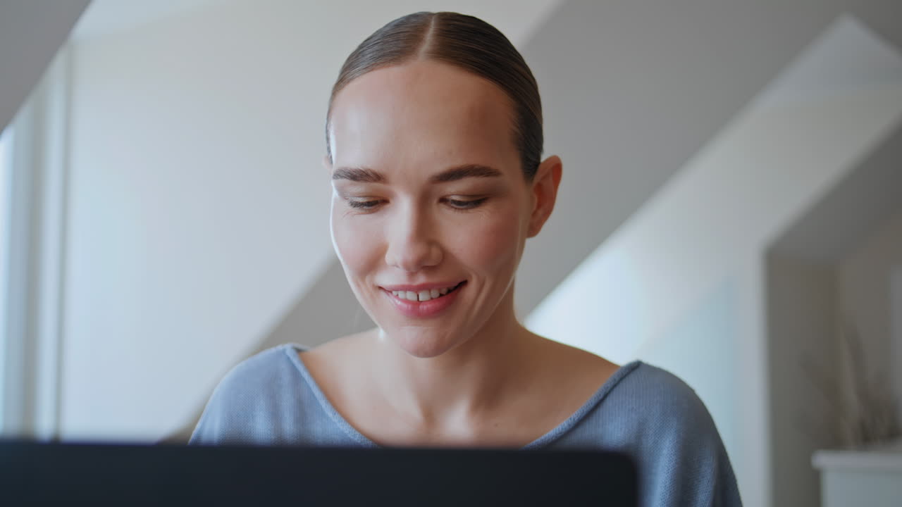 Glad medarbejder ser på en bærbar skærm med et smil derhjemme, nærbillede. Kvinde arbejder