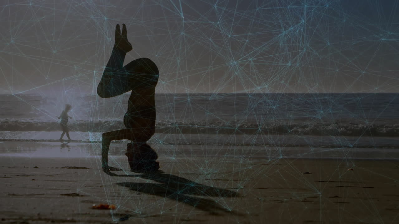 Yogi holding headstand on wet sand by ocean, glowing technology network overlay unfolding