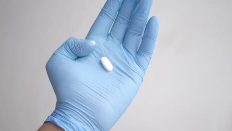 mano con guantes azules sosteniendo una píldora blanca