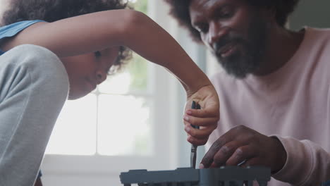primer plano de un niño preadolescente construyendo un juguete de kit usando alicates, su padre ayudándolo, primer plano, enfoque en primer plano