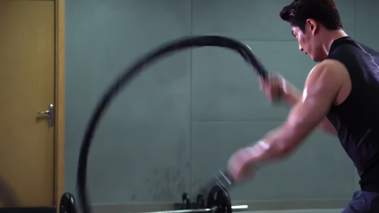 Strong Muscular sportsman sportswear bodybuilder weightlifter in fitness top and leggings doing battle rope workout in empty gymnasium