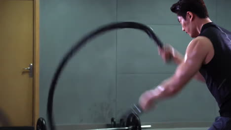 strong muscular sportsman sportswear bodybuilder weightlifter in fitness top and leggings doing battle rope workout in empty gymnasium