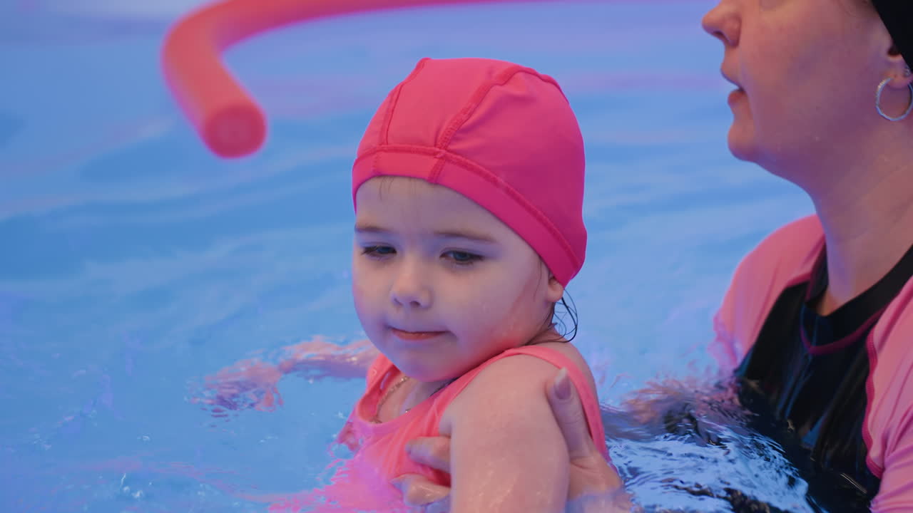 Caregiver gently holds white baby in pool, letting child freely move arms and legs through cool water, expressing innocence, joy, and calm interaction while exploring safe swimming environment