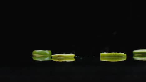 rings of fresh green lime sliced fall on the glass with splashes of water in slow motion.