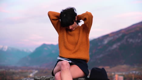 brunette woman styling her hair under a hat during sunset