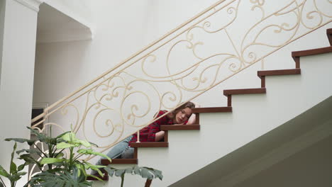 exhausted woman lies on own apartment staircase. vulnerable lady paralyzed by hard panic attack at home. pensive woman suffers from depression disorder