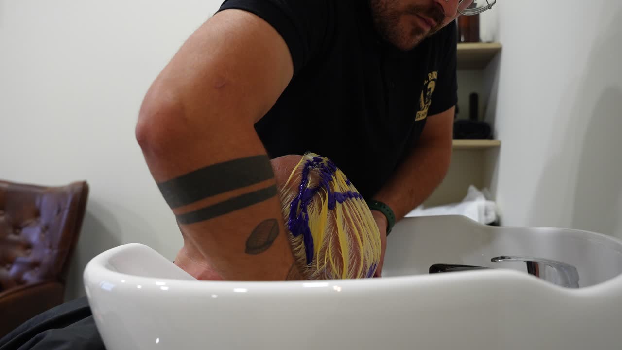 Close up shot of hairdresser massaging purple shampoo into client’s yellow-toned hair to tone after bleaching