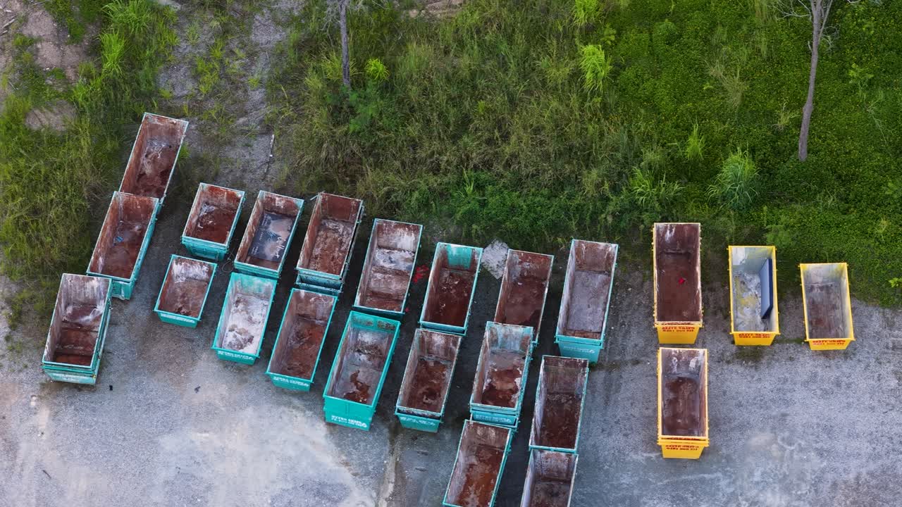 Drone shot pans across rows of colorful metal waste containers in an industrial quarry yard