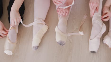 Kaukasische-Balletttänzerinnen-Sitzen-Zusammen-Auf-Dem-Boden-Und-Unterhalten-Sich,-Während-Sie-Ballettschuhe-Binden