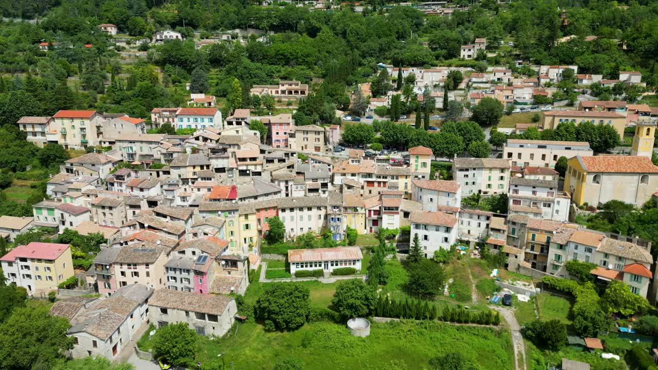 Bird’s-eye view of a sunlit village in the south of France, with colorful rooftops and scenic nature.