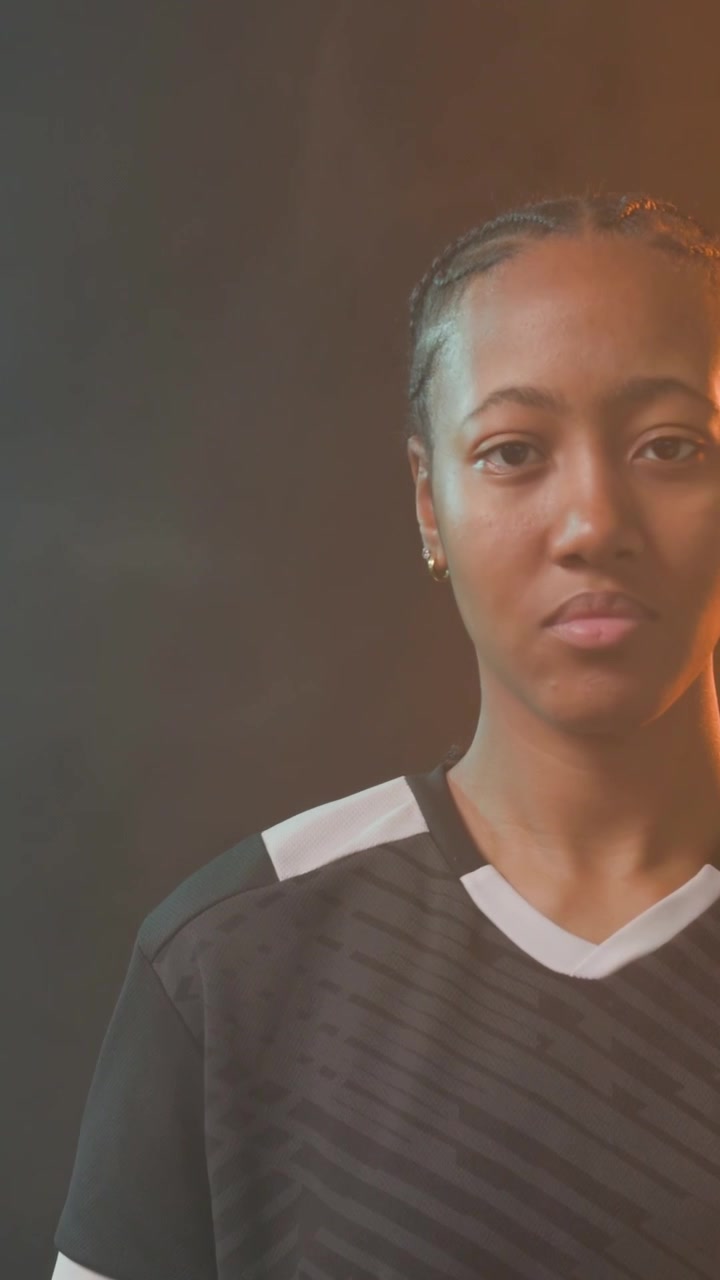 Video verticale: La telecamera si muove verso l'alto mostrando una donna che palleggia un pallone da calcio su erba sintetica, in tenuta nera per una promozione.