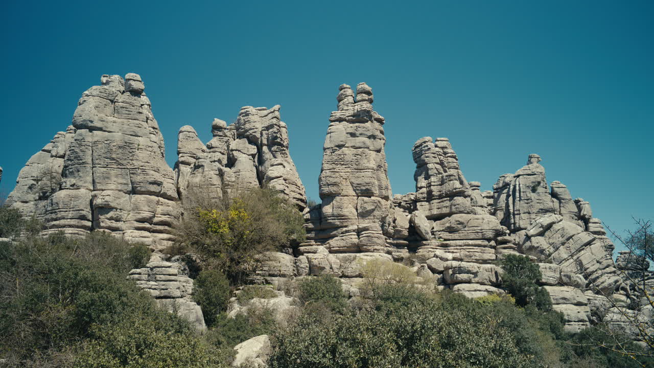 Ampia veduta di caratteristiche formazioni rocciose calcaree a El Torcal de Antequera, Spagna, che mostrano forme carsiche uniche, terreno accidentato e motivi naturali sotto un cielo azzurro brillante.