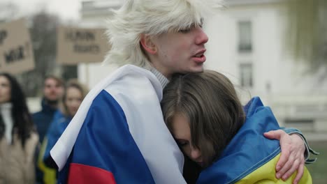 un joven caucásico con bandera rusa abrazando a una joven caucásica con bandera ucraniana.