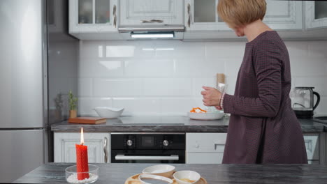 la mujer prepara la cena en una cocina moderna con una vela roja encendida en la encimera, arregla los platos e ingredientes, creando una atmósfera cálida y acogedora con la luz de las velas parpadeantes y una decoración acogedor.