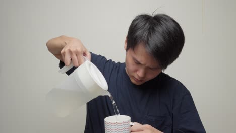 young man pours refreshing water from transparent beaker, drinks from mug