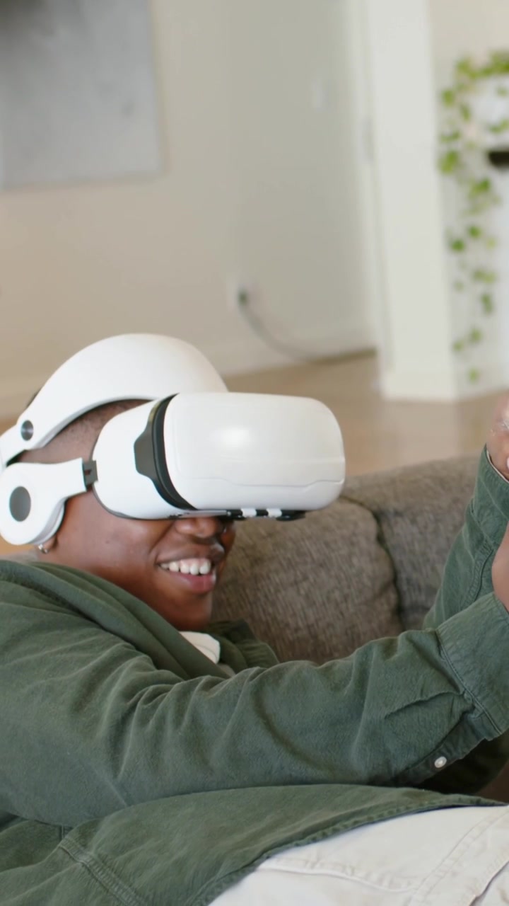 Video verticale: Reazione alla VR, uomo in maglietta verde che afferra il telecomando ridendo a casa, visore bianco