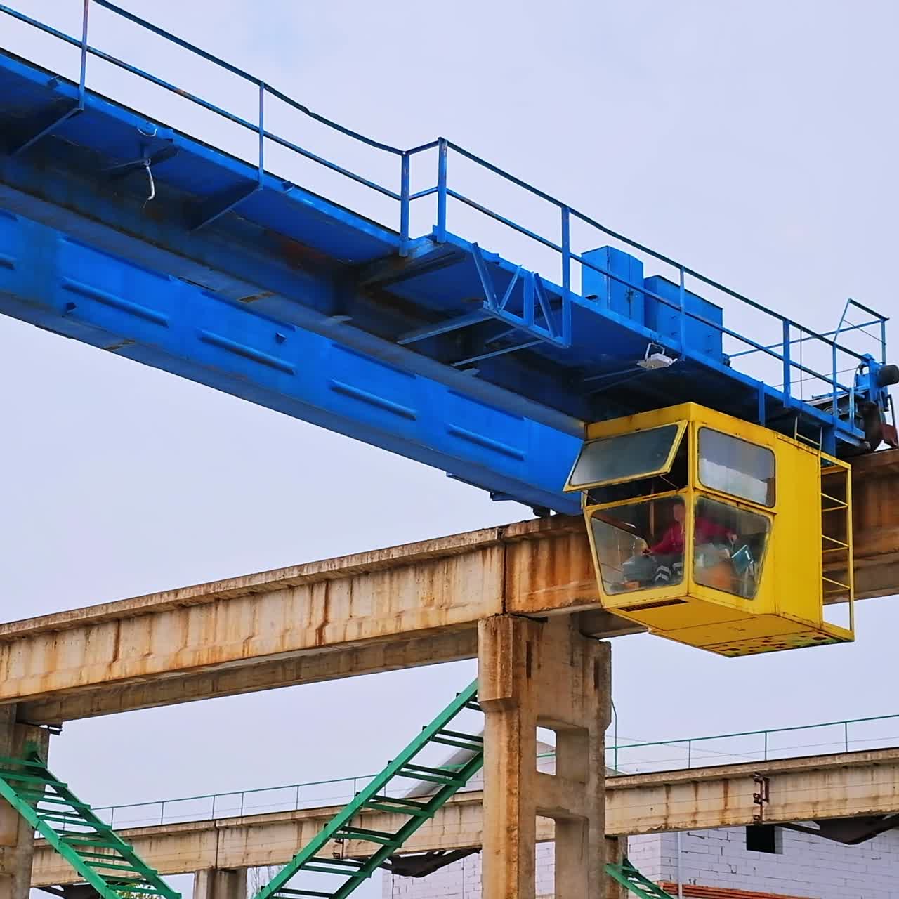 Yellow booth with a working person inside. Construction crane machinery at the backdrop of grey sky