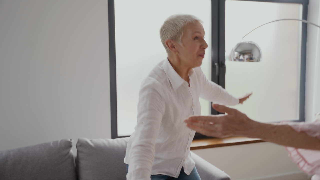 пожилая женщина машет рукой и обнимает двух пожилых друзей в гостиной