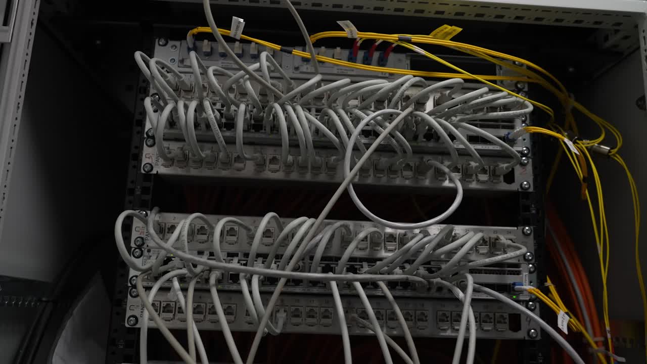 Network cable cabinet with multiple patch panels and bundled wiring inside a technical equipment rack. White and yellow cables visible in an electrical or communication setup