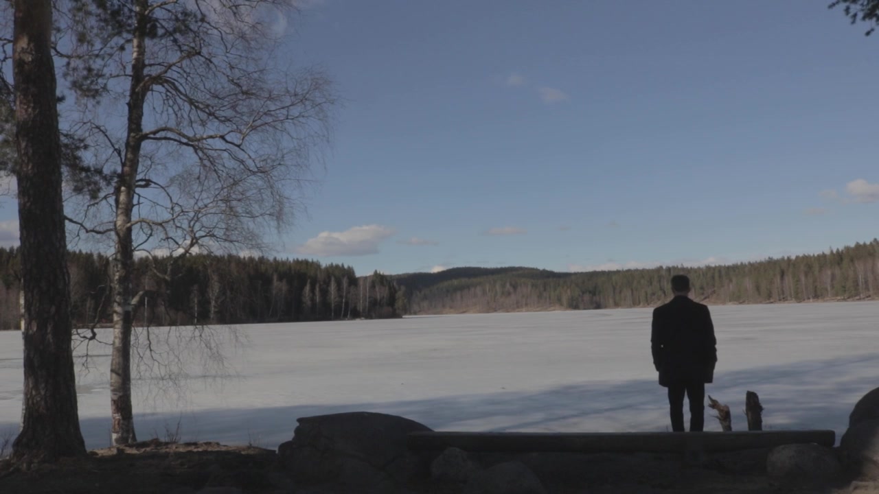 Man som blickar ut över den frusna sjön Sognsvann i Oslo, omgiven av skog en solig vårdag.