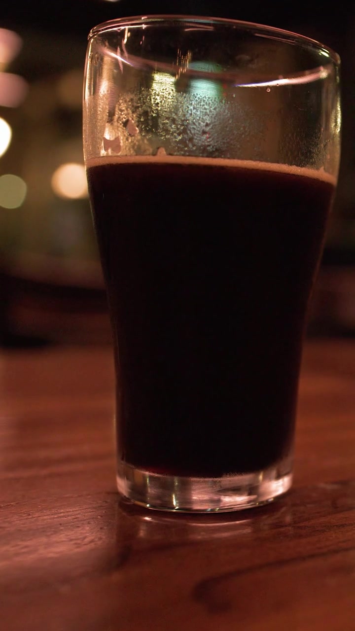 A vertical shot of a dark stout beer glass on a polished wooden table.