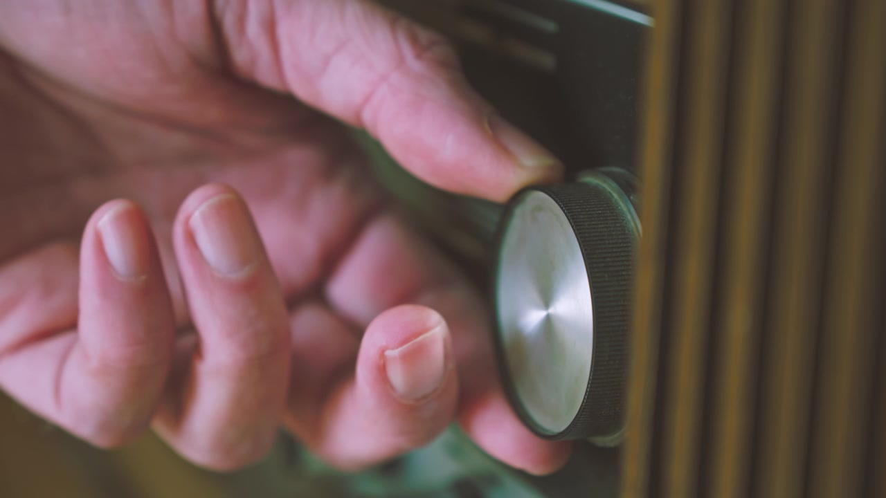 Close-up de mão ajustando o seletor de sintonia em um rádio-vitrola alemão vintage. Adequado para tecnologia de áudio retrô, história da radiodifusão e visuais de mídia vintage