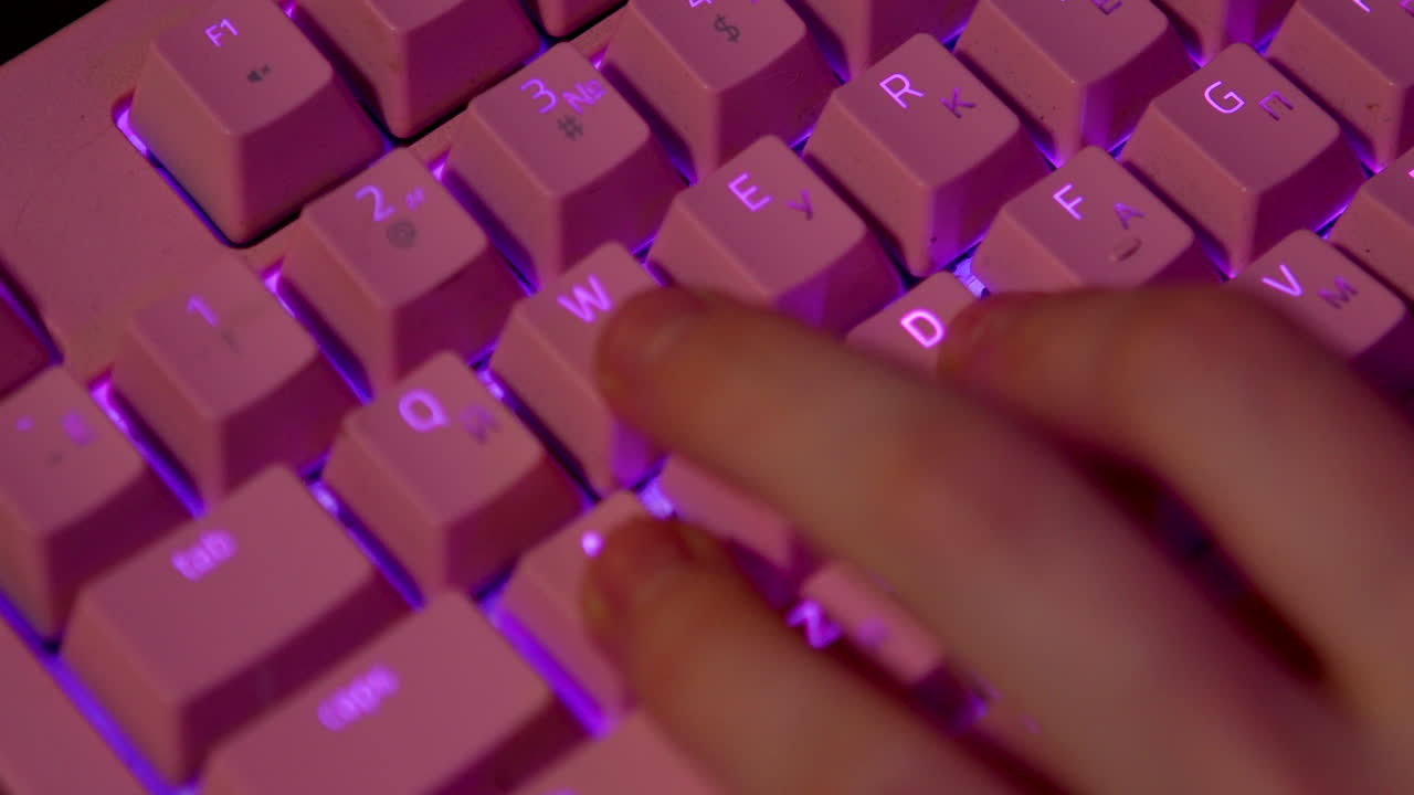 Closeup of hands typing on a pink illuminated keyboard