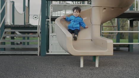 Cheerful-Asian-kid-descends-from-the-slide-on-the-playground