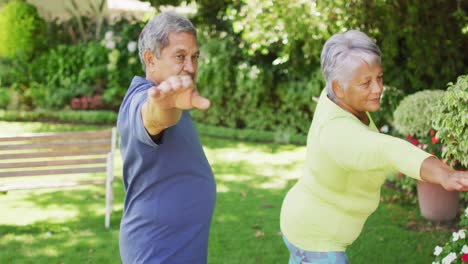 video de una relajada pareja de ancianos biraciales practicando yoga en el jardín