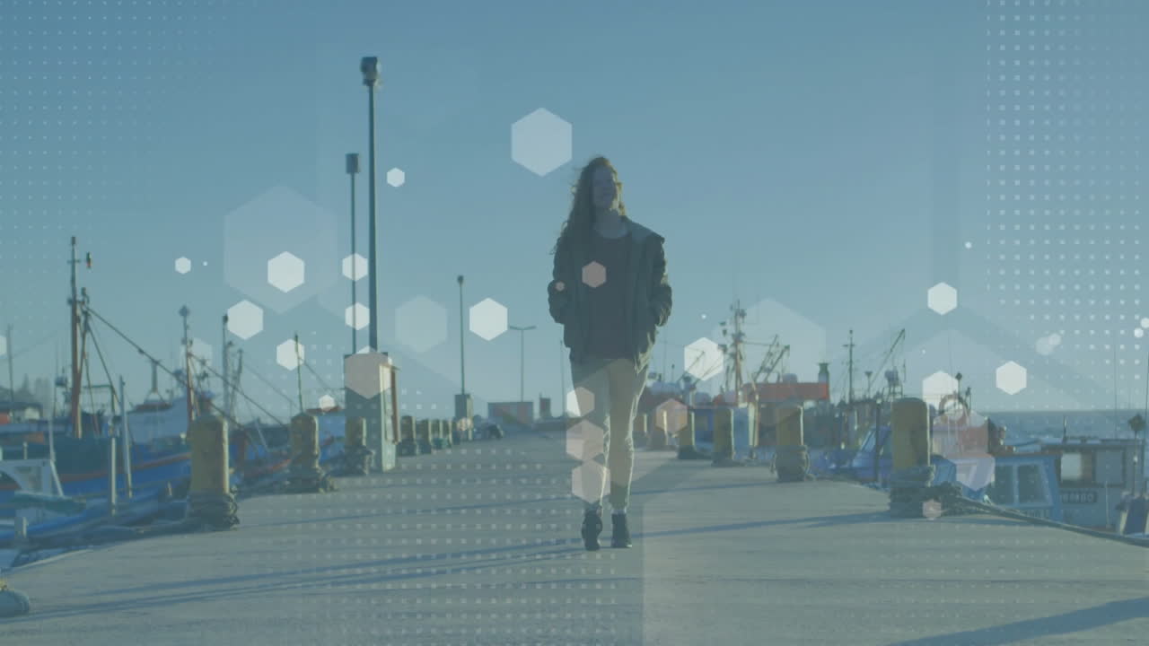 Woman walking down concrete harbor pier, showing technology hexagonal data overlays on bollards