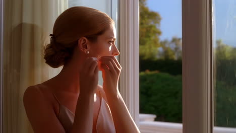 woman putting on earrings by a window in soft light