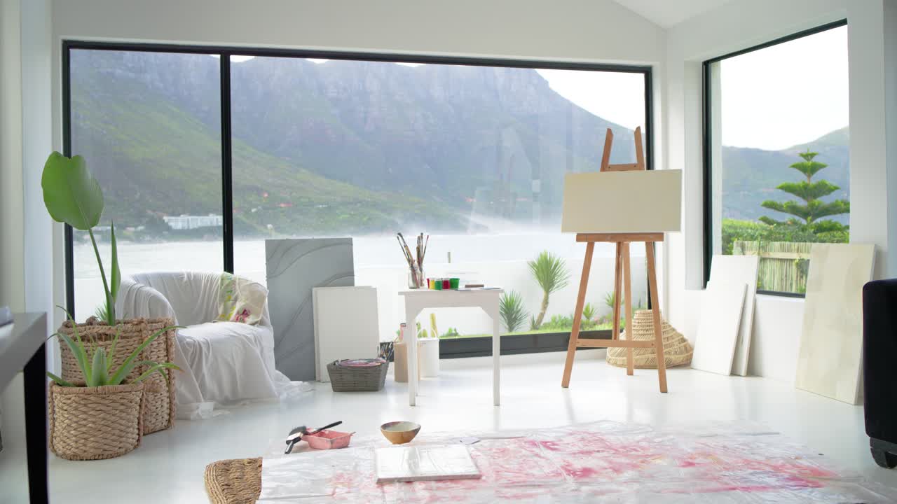 La telecamera effettua una lenta panoramica, rivelando uno studio d'arte con un cavalletto di legno, colori e un tappeto che mostra l'area di lavoro