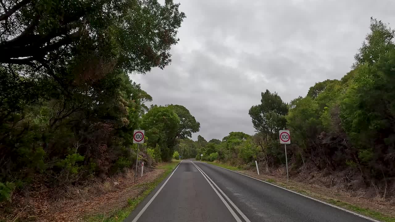 Forward-facing hyperlapse captures a winding drive on the Great Ocean Road, Victoria, Australia, through lush forests and open farmland under overcast skies