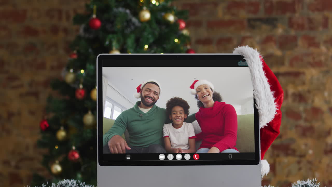 familia feliz con sombreros de santa claus en la llamada de video del monitor de la computadora, con decoraciones de navidad y árbol