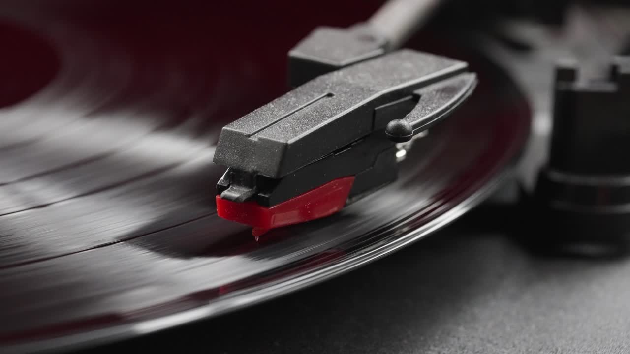 Extreme close-up view of black vinyl spinning on a red vintage record player's stylus head
