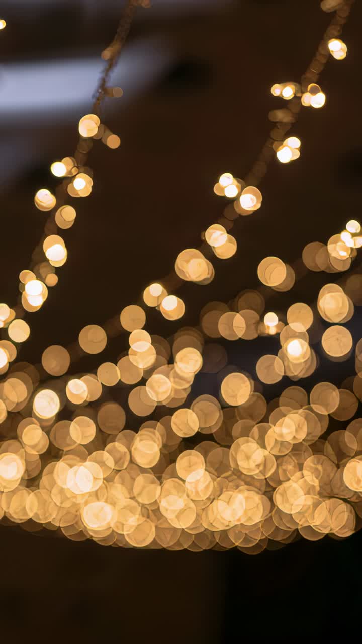 Vertical video: Tilting camera showing string lights making dynamic bokeh at venue, with wires