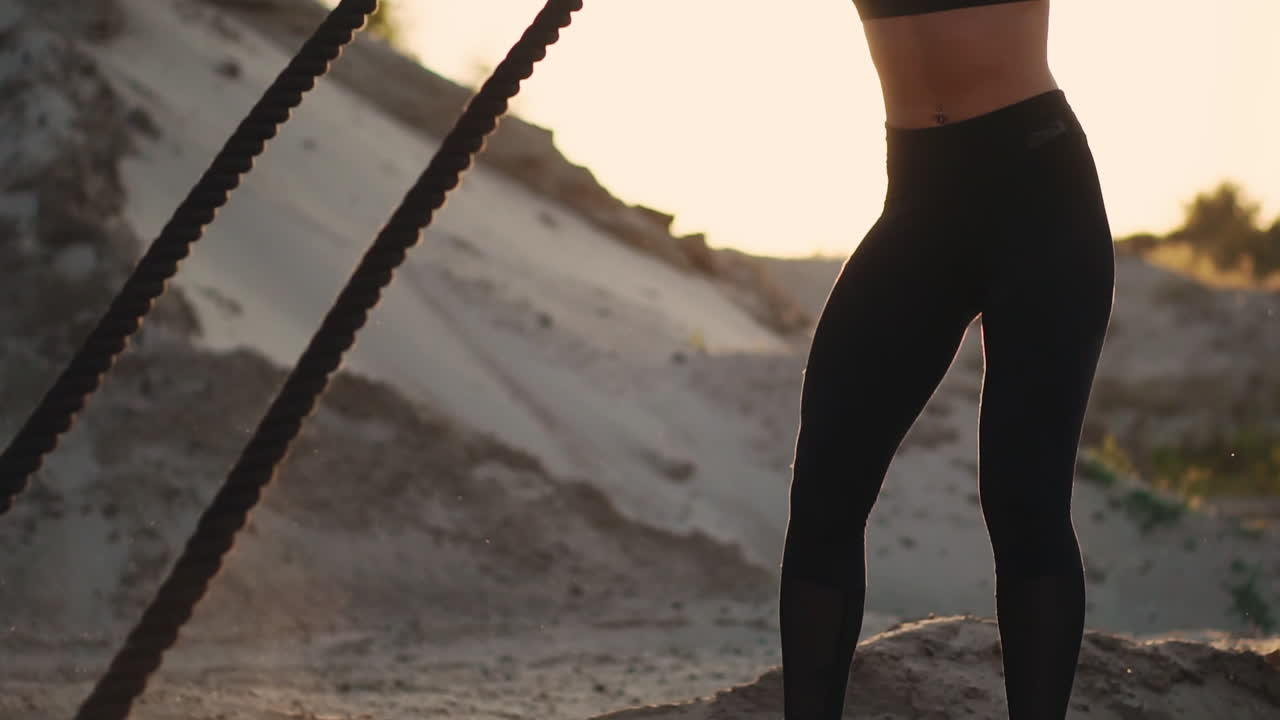 Female athlete training outdoors around the sand hills at sunset. Active physical activity workout. crossfit. The girl has a rope on the ground