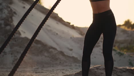 female athlete training outdoors around the sand hills at sunset. active physical activity workout. crossfit. the girl has a rope on the ground