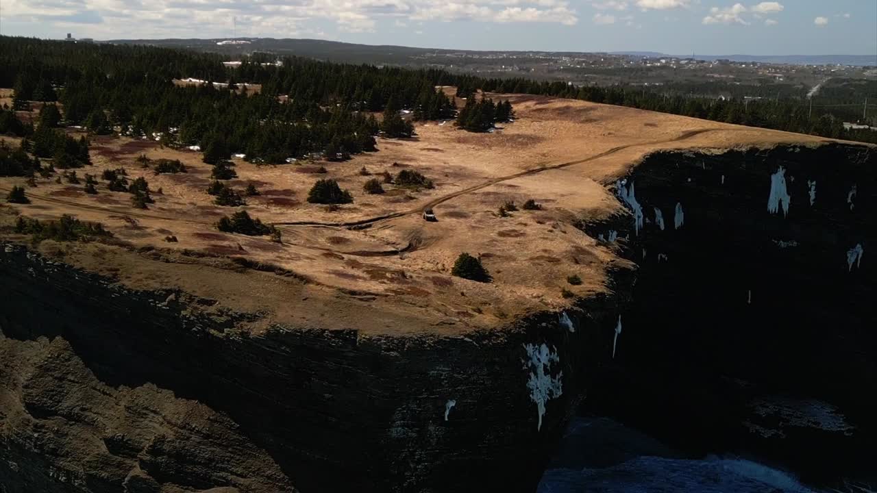 вращающийся дроновый снимок внедорожника, движущегося по краю 300-футовых скал
