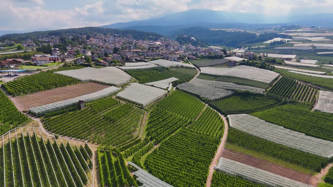 Aerial view of agricultural fields near Coredo, featuring apple orchards, greenhouses, and rolling hills in the Trentino region of Italy