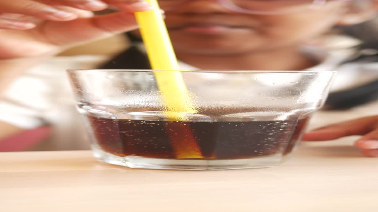 primer plano de una persona bebiendo refresco de un vaso con una pajita amarilla.